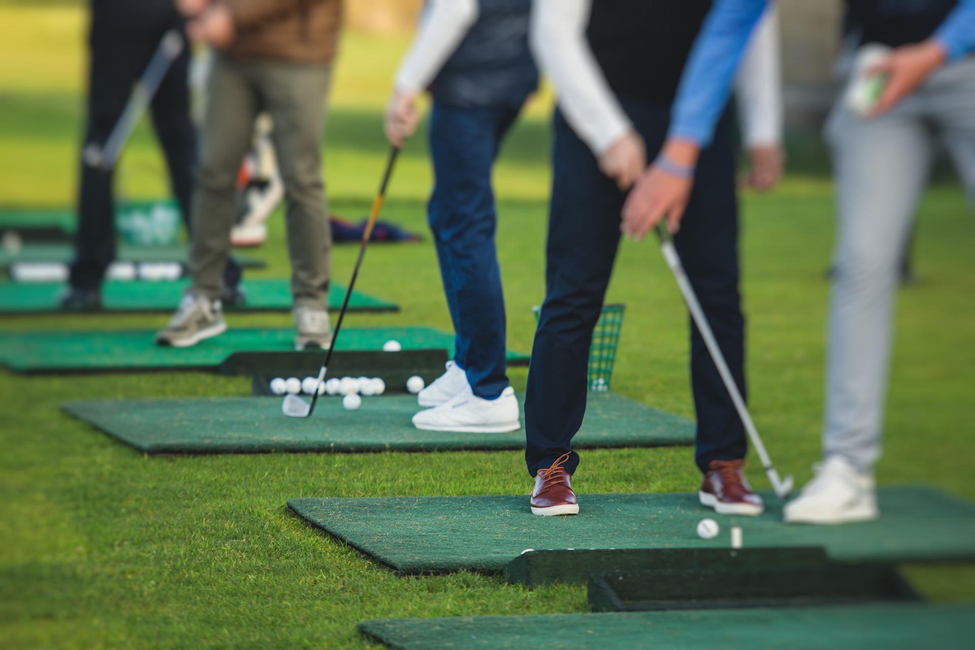 Group of golfers practicing and training golf swing on driving range practice, men playing on golf course, golf ball at golfing complex club resort