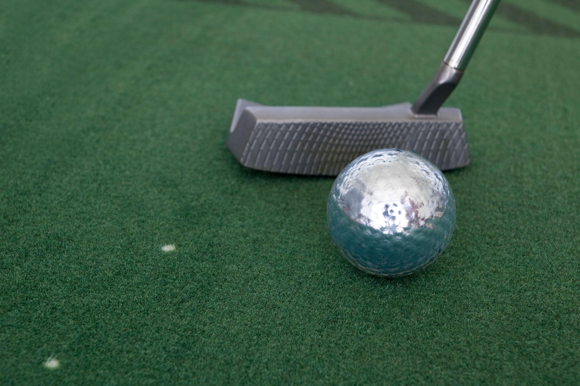 Silver golf ball and putter on practice mat