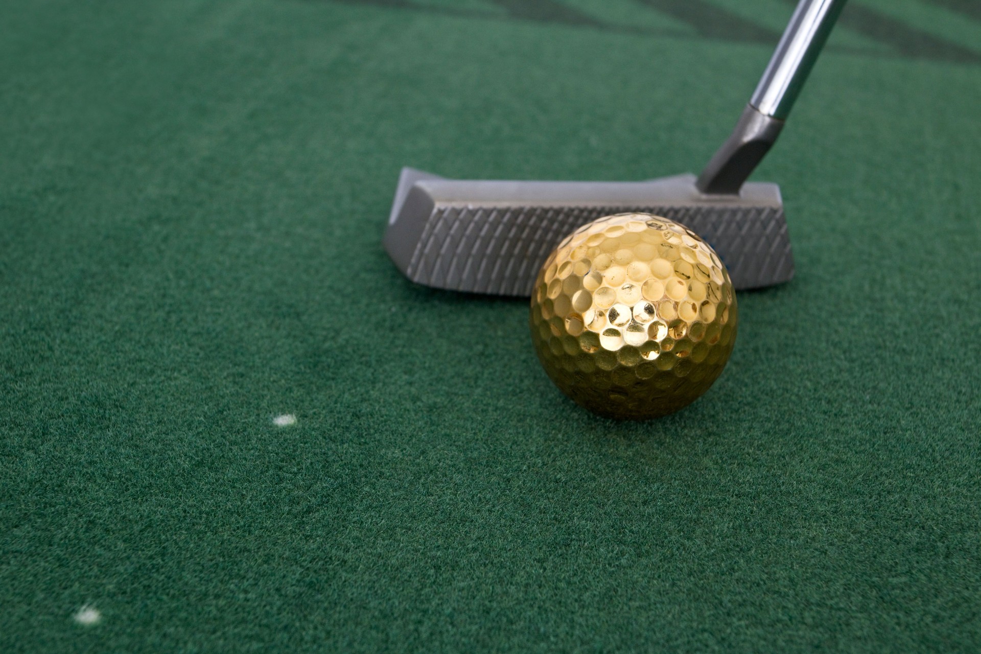 Gold golf ball and putter on practice mat